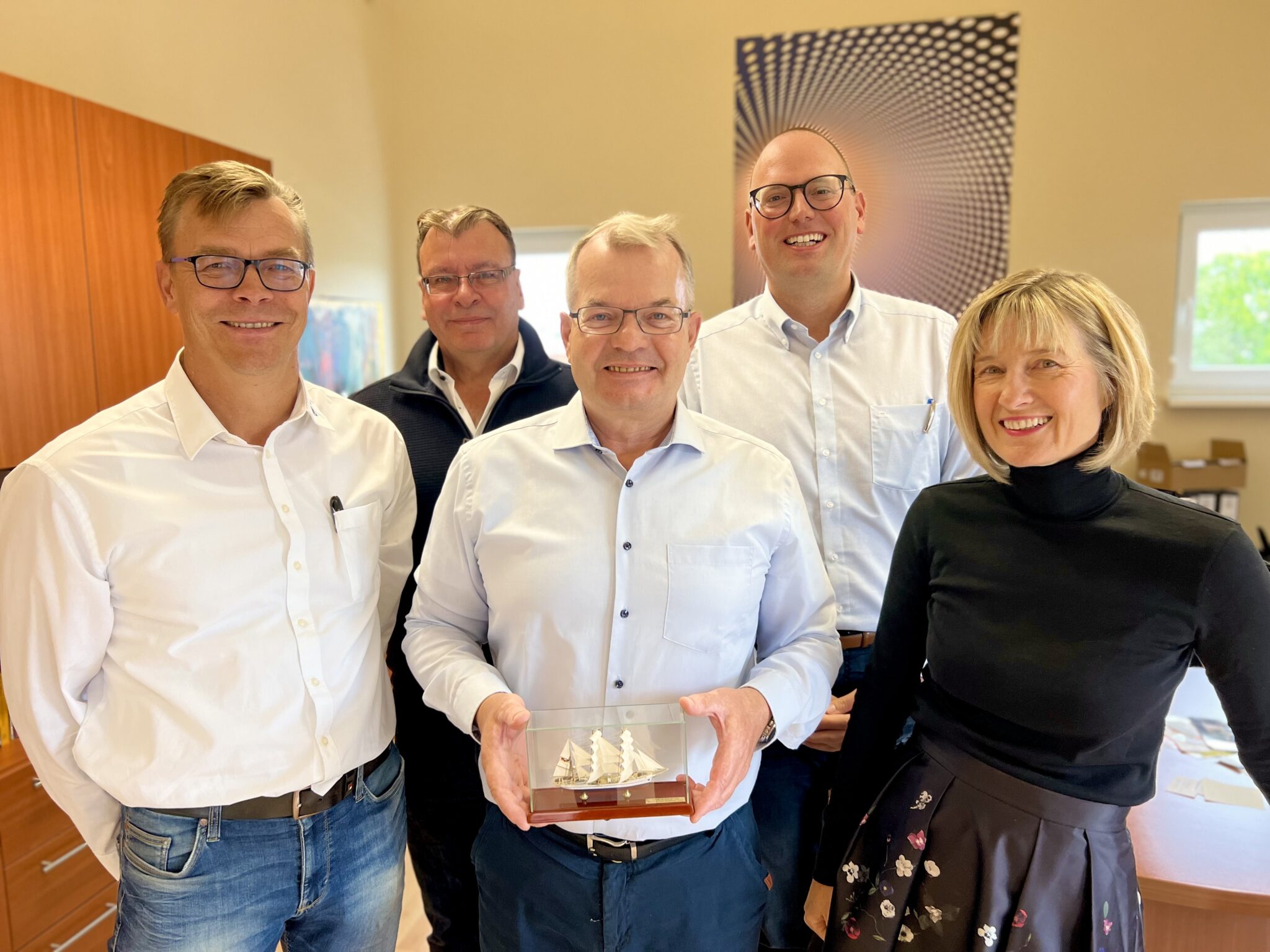 Geschäftsführer Bernhard Etzelmüller von Wiedenmann Seile hält das Modell der Gorch Fock II in einer Glasvitrine, umgeben von Mitgliedern der Geschäftsleitung, das ihn zu seinem 40-jährigen Jubiläum gratuliert.