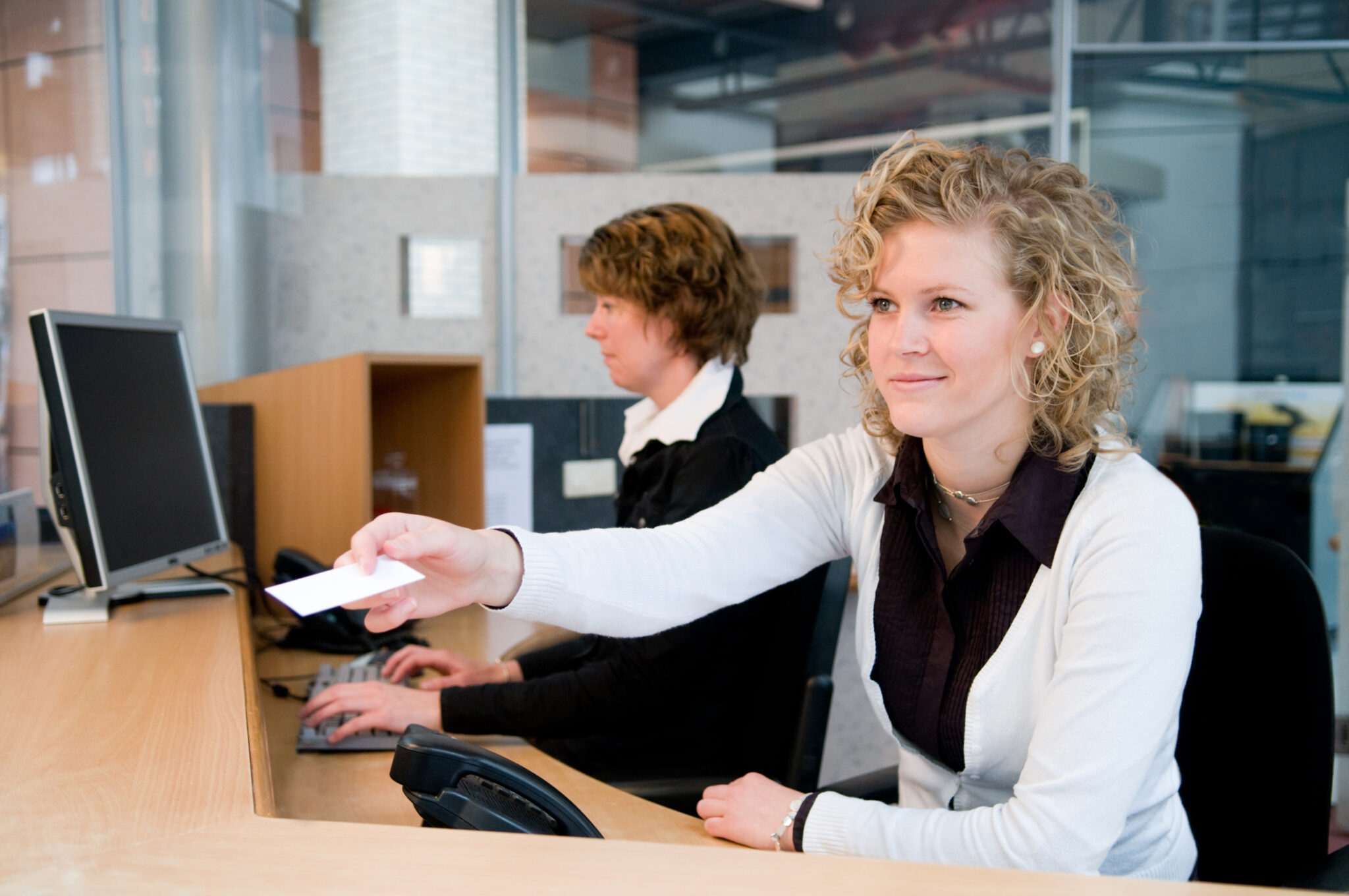 Mitarbeiterinnen am Empfang begrüßen Kunden in einem modernen Bürogebäude.
