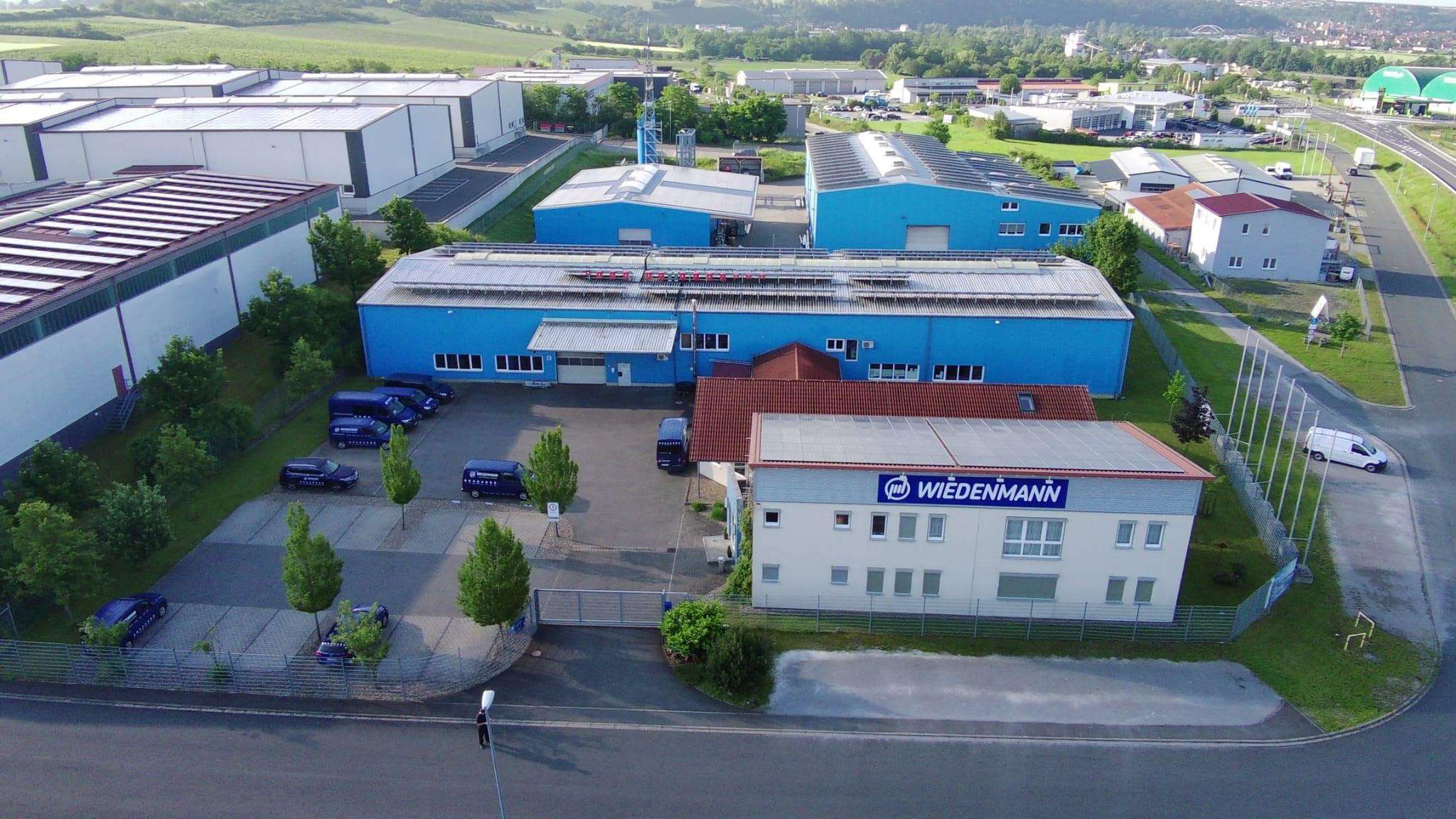 Luftaufnahme des Firmenhauptsitzes von Wiedenmann-Seile GmbH mit blauen Lagerhallen und Verwaltungsgebäude.
