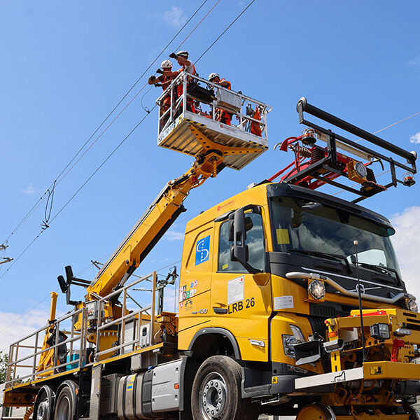 Hubarbeitsbühne auf Spezial-LKW bei Arbeiten an einer Bahnoberleitung, mehrere Fachkräfte montieren Oberleitungsleitungen über der Bahnstrecke