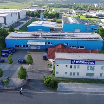 Luftaufnahme des Firmenhauptsitzes von Wiedenmann-Seile GmbH mit blauen Lagerhallen und Verwaltungsgebäude.